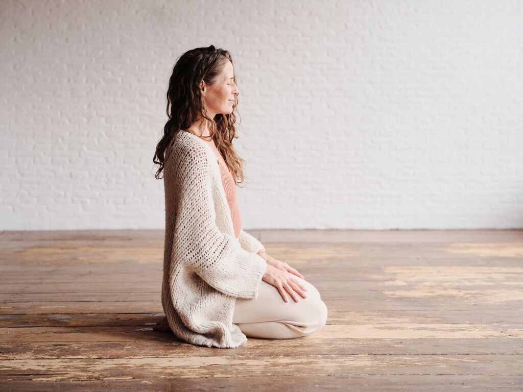 Sanne sitting in meditation on a wooden floor