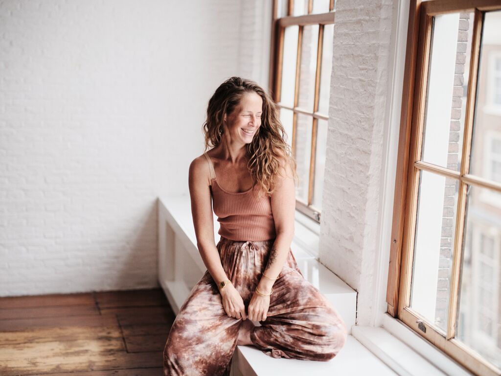 Sanne laughing on a windowsill in a bright studio